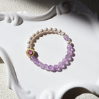 Pearl and purple beaded bracelet with a pink gemstone on a decorative white base.