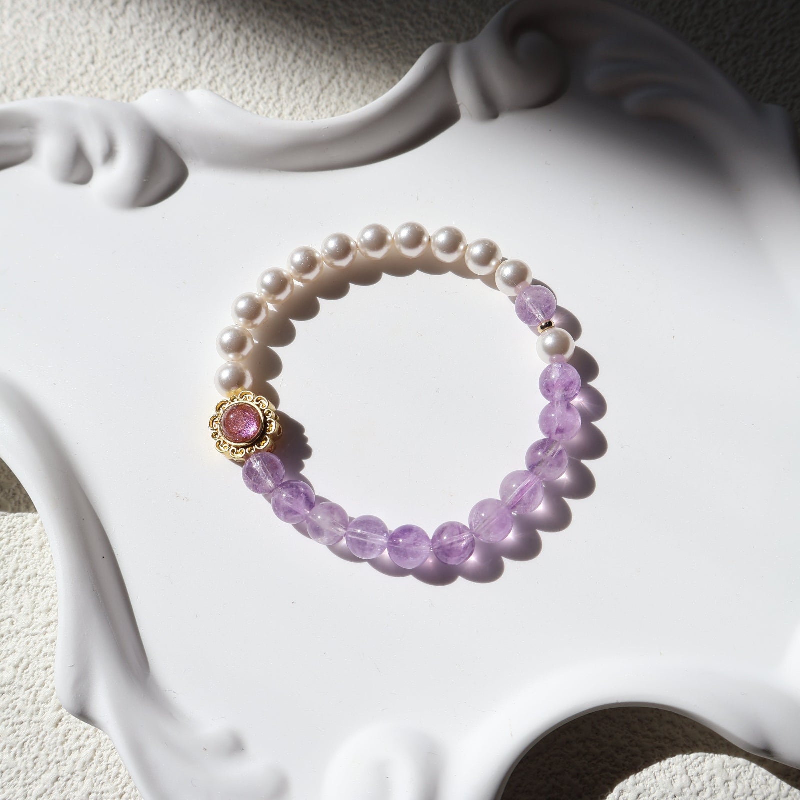 Pearl and purple beaded bracelet with a pink gemstone on a decorative white base.