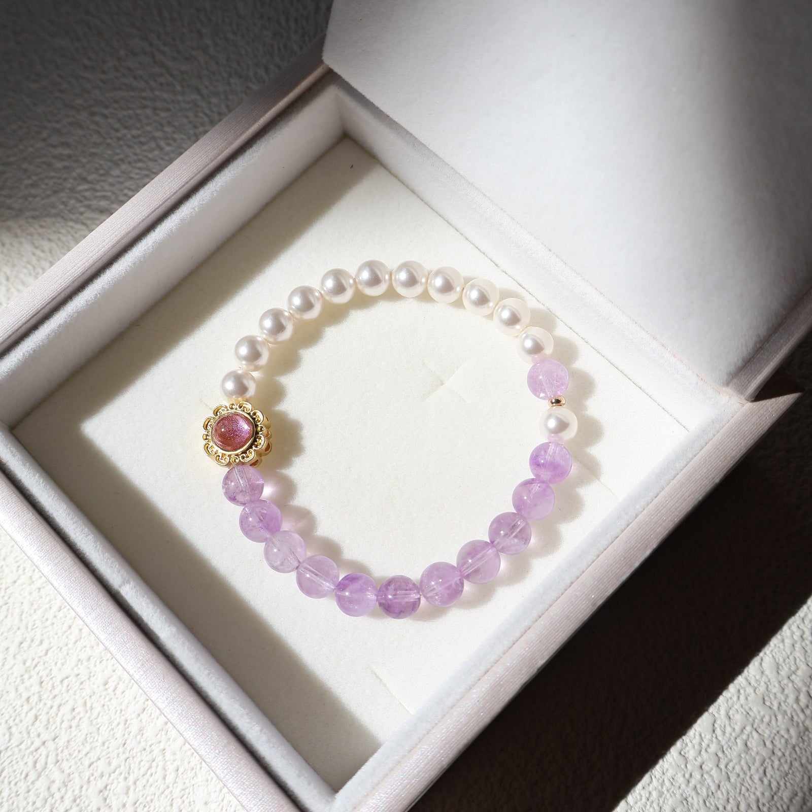 Bracelet with purple beads and a pink gemstone in a white box