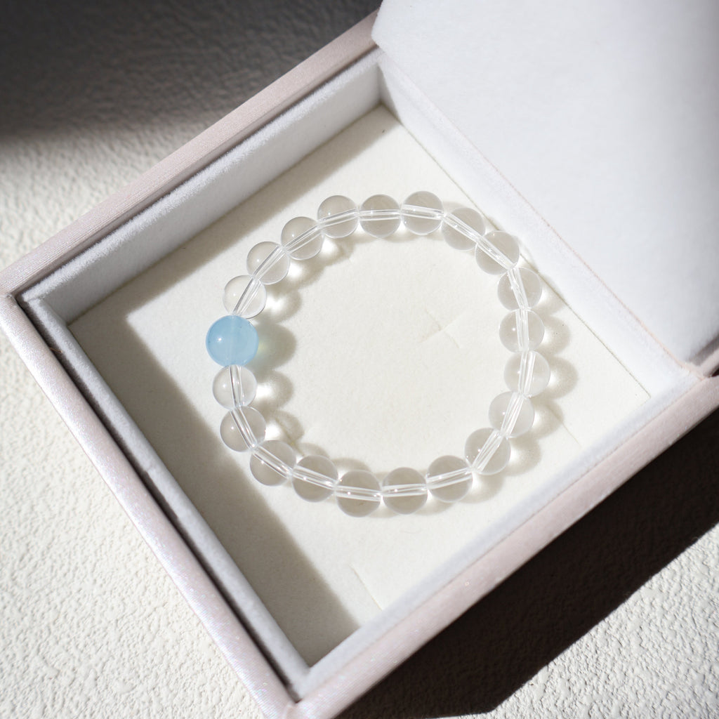 Clear beaded bracelet with a blue accent stone in a white box
