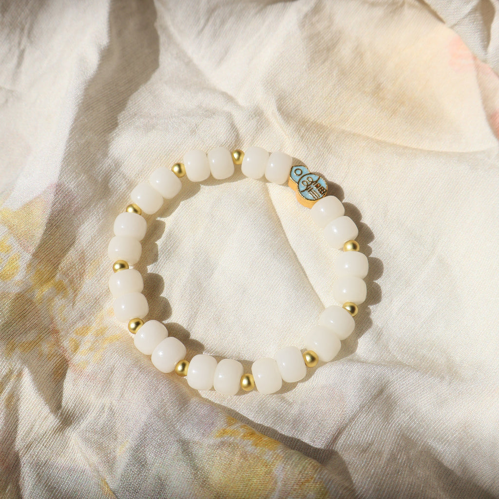 White beaded bracelet with gold accents on a textured fabric background