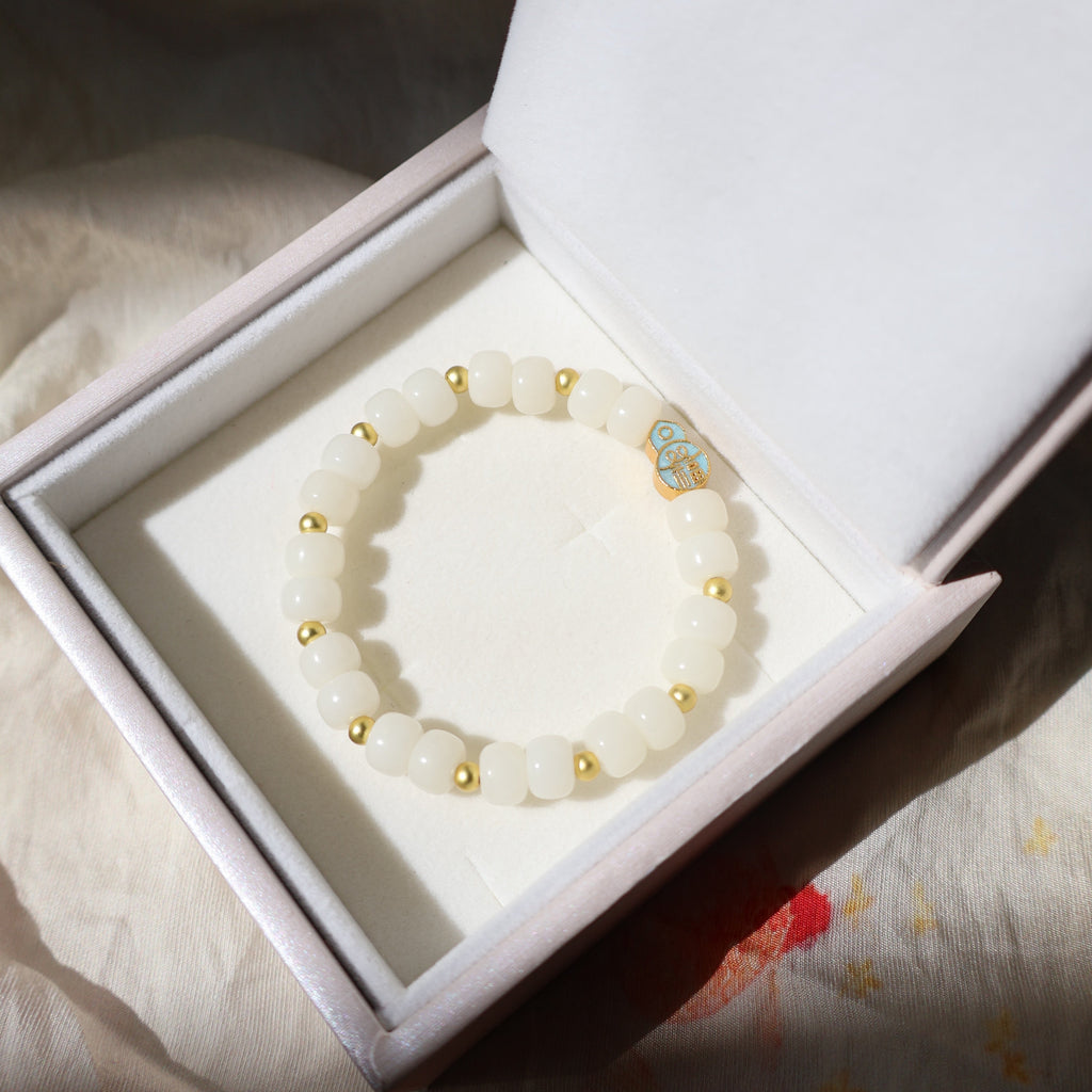 White beaded bracelet with gold accents in a white box on a floral fabric background