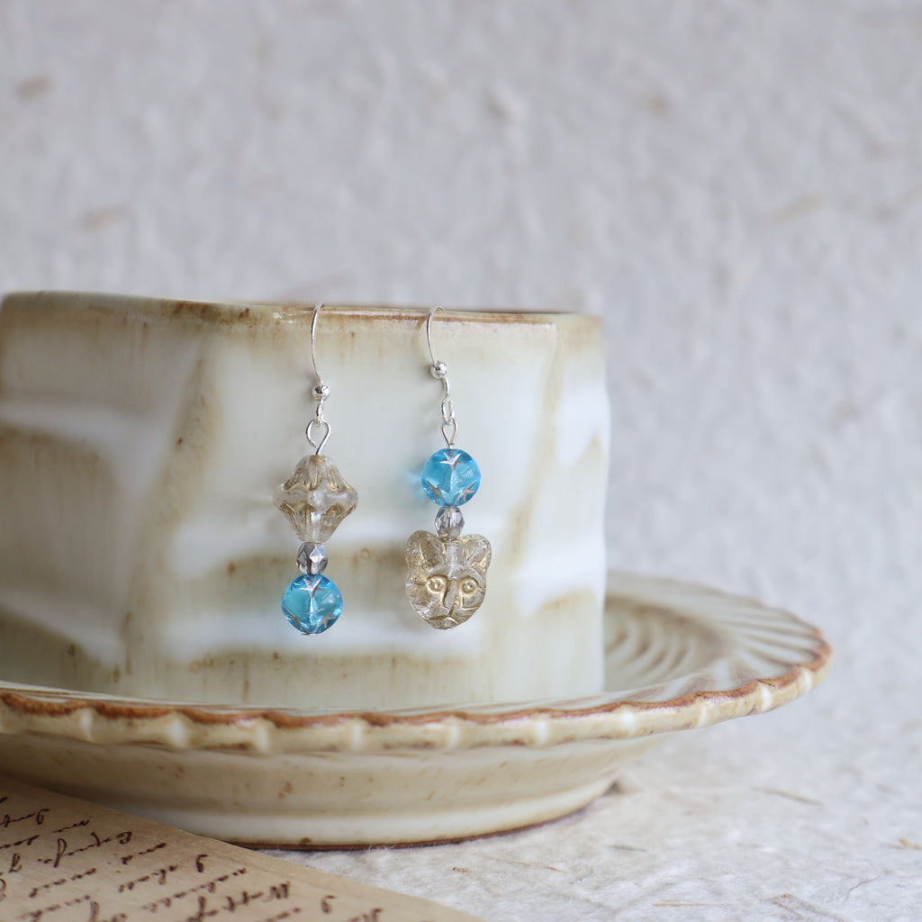 Pair of earrings with blue gemstones and silver hooks on a shell.