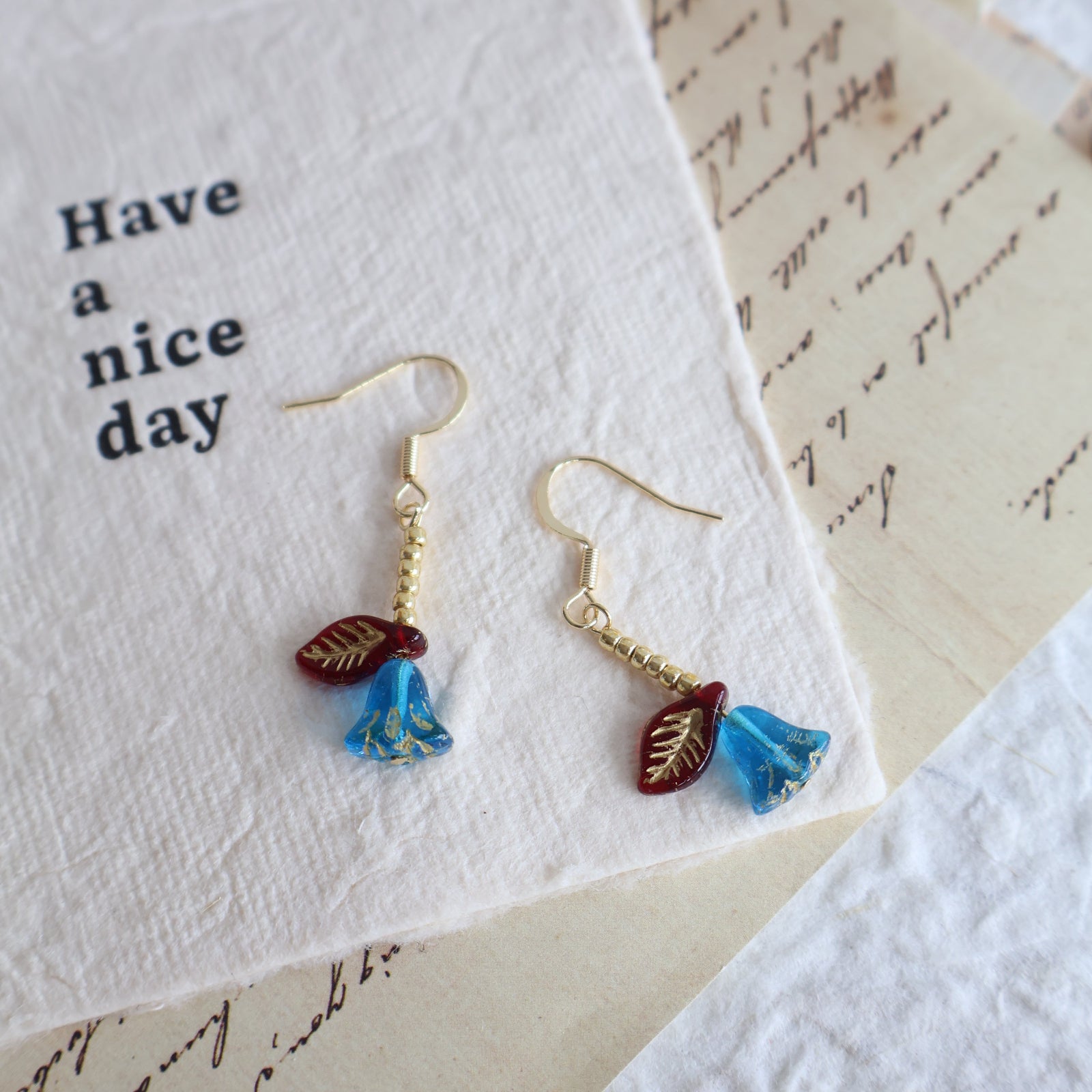 Gold earrings with blue and red floral designs on a textured paper background