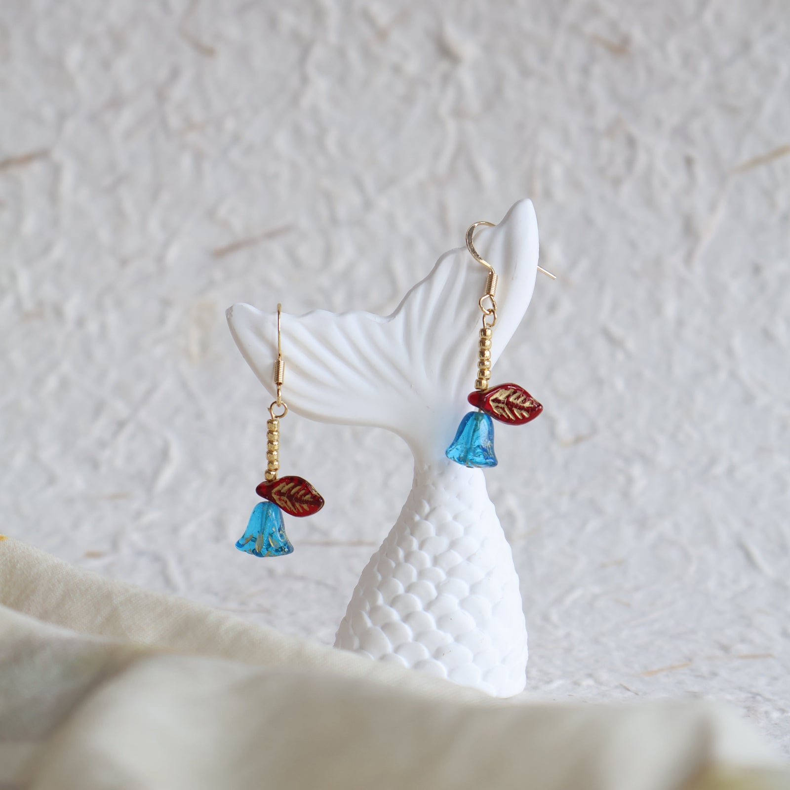 Earrings with blue and red leaf-like charms on a textured white surface