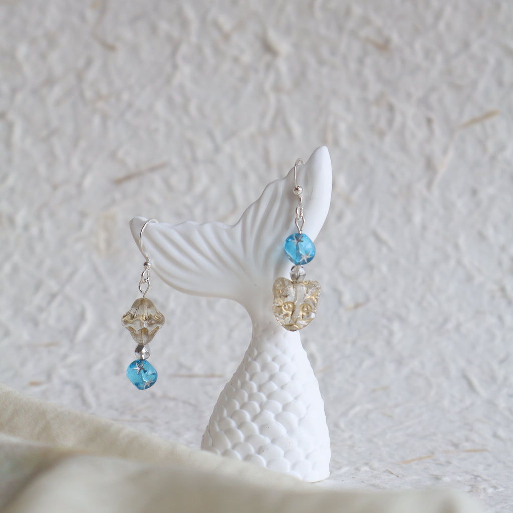Mermaid tail earrings with blue and gold beads on a textured white background
