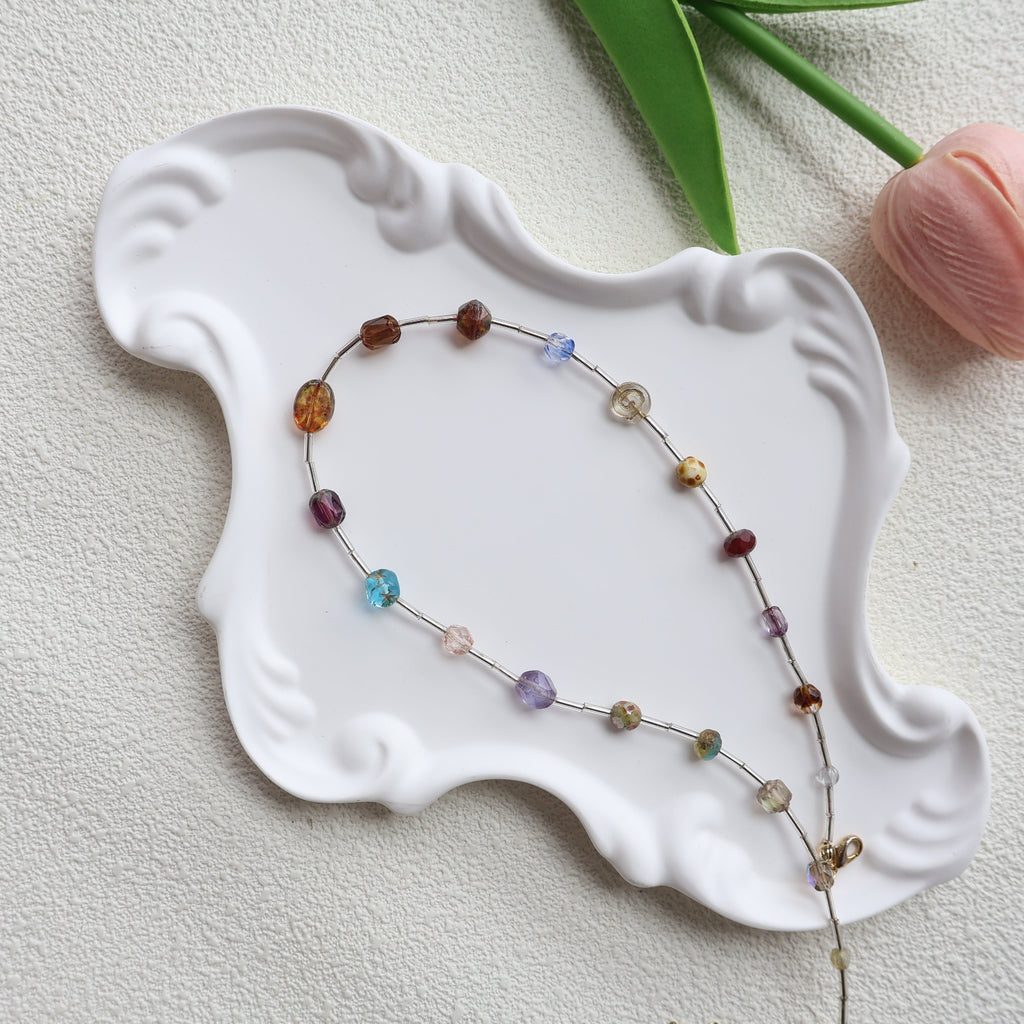 Multicolored beaded necklace on a white decorative plate with a light background