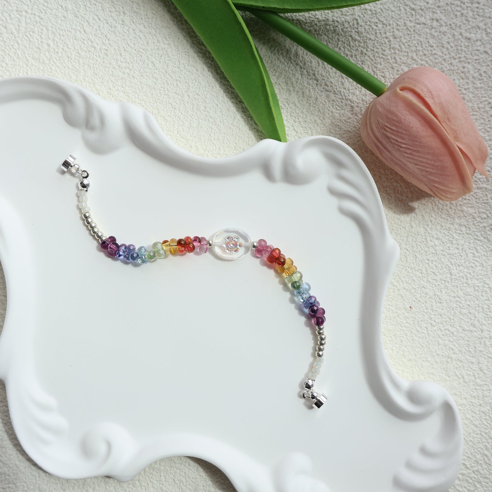 Colorful beaded bracelet on a white decorative stand with a pink tulip in the background