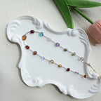 Multicolored beaded necklace on a white decorative plate with green leaves in the background