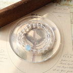 Clear circular object with leaf and blue stone on an open book