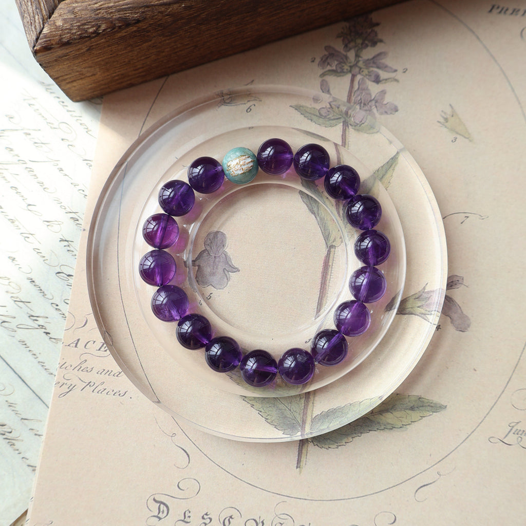 Purple beaded bracelet on a decorative plate with a wooden surface and paper in the background