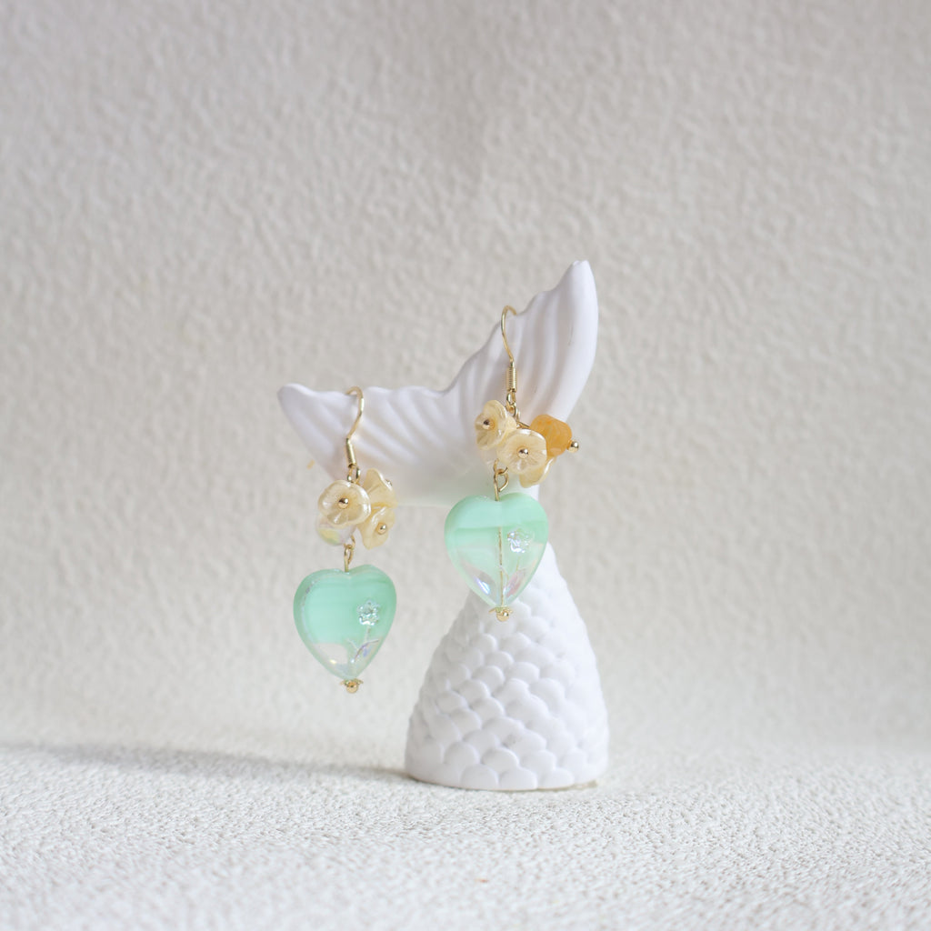 Shell earrings with green and gold beads on a textured white background