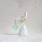 Shell earrings with green and gold beads on a textured white background