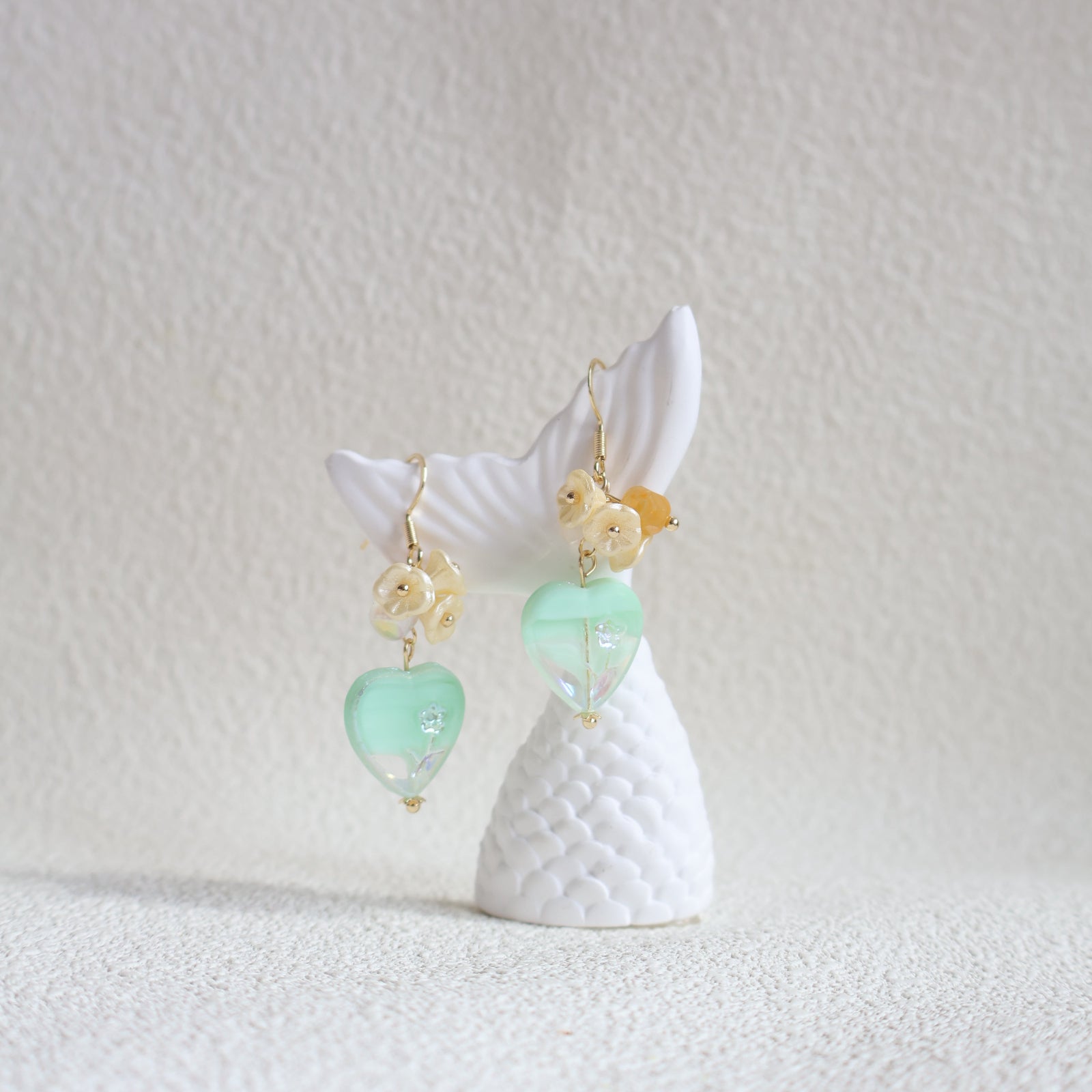 Shell earrings with green and gold beads on a textured white background