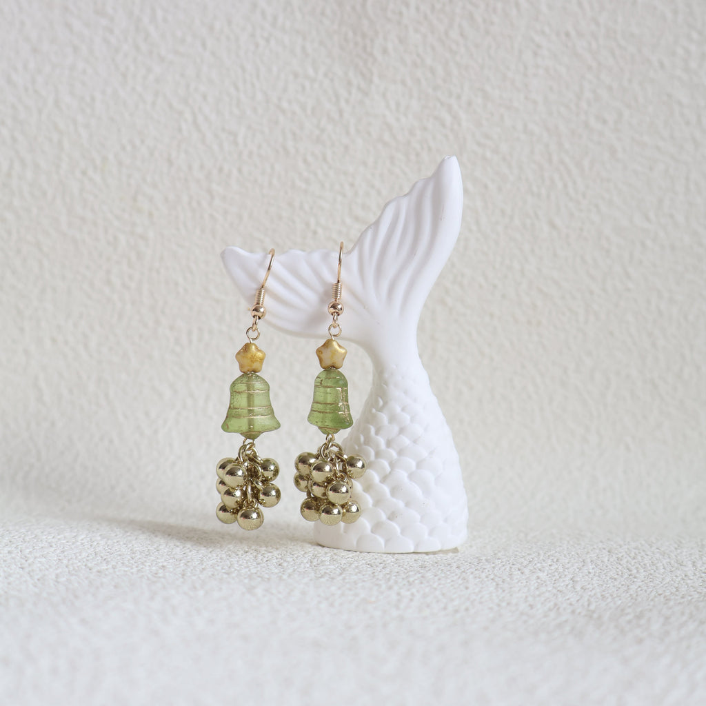 Mermaid tail with green and gold beaded earrings on a textured white background