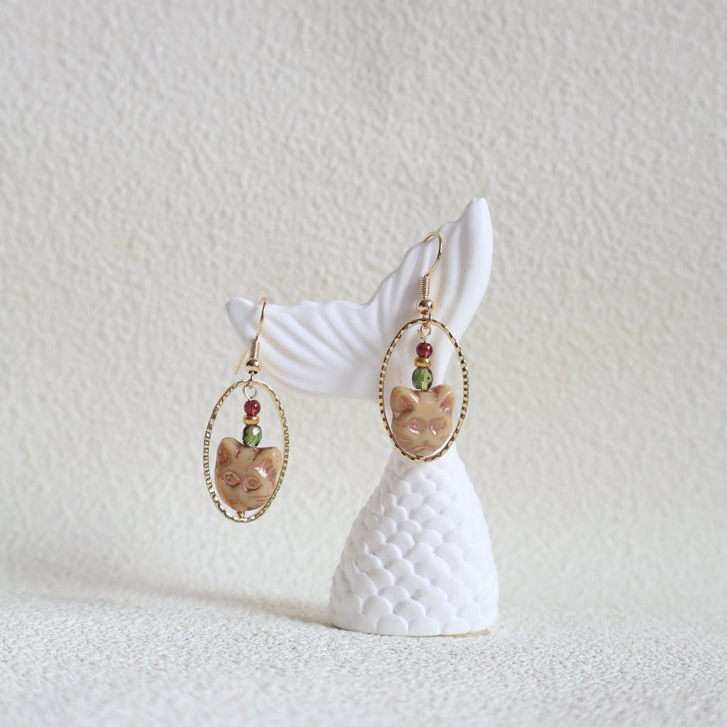 Earring with white shell design and gold and gemstone accents on a textured white background