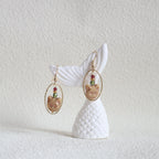 Earring with white shell design and gold and gemstone accents on a textured white background