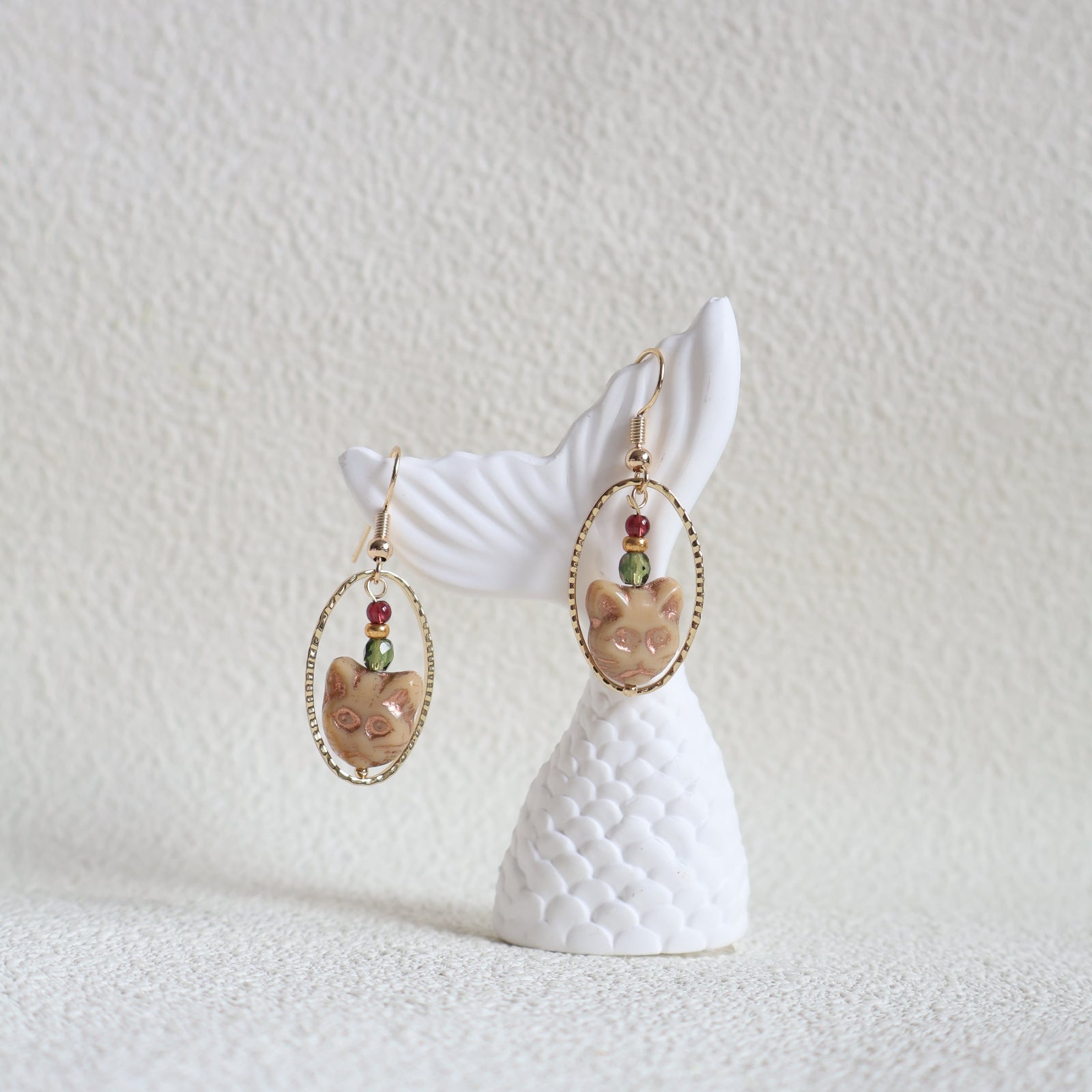 Earring with white shell design and gold and gemstone accents on a textured white background