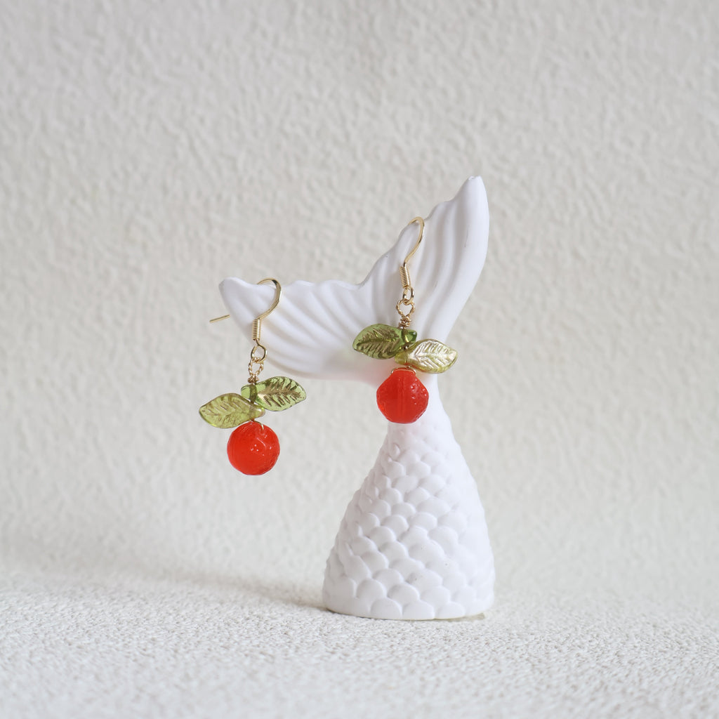 White fish-shaped earring with red and green accents on a textured white background