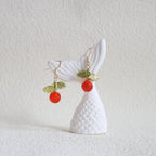White fish-shaped earring with red and green accents on a textured white background