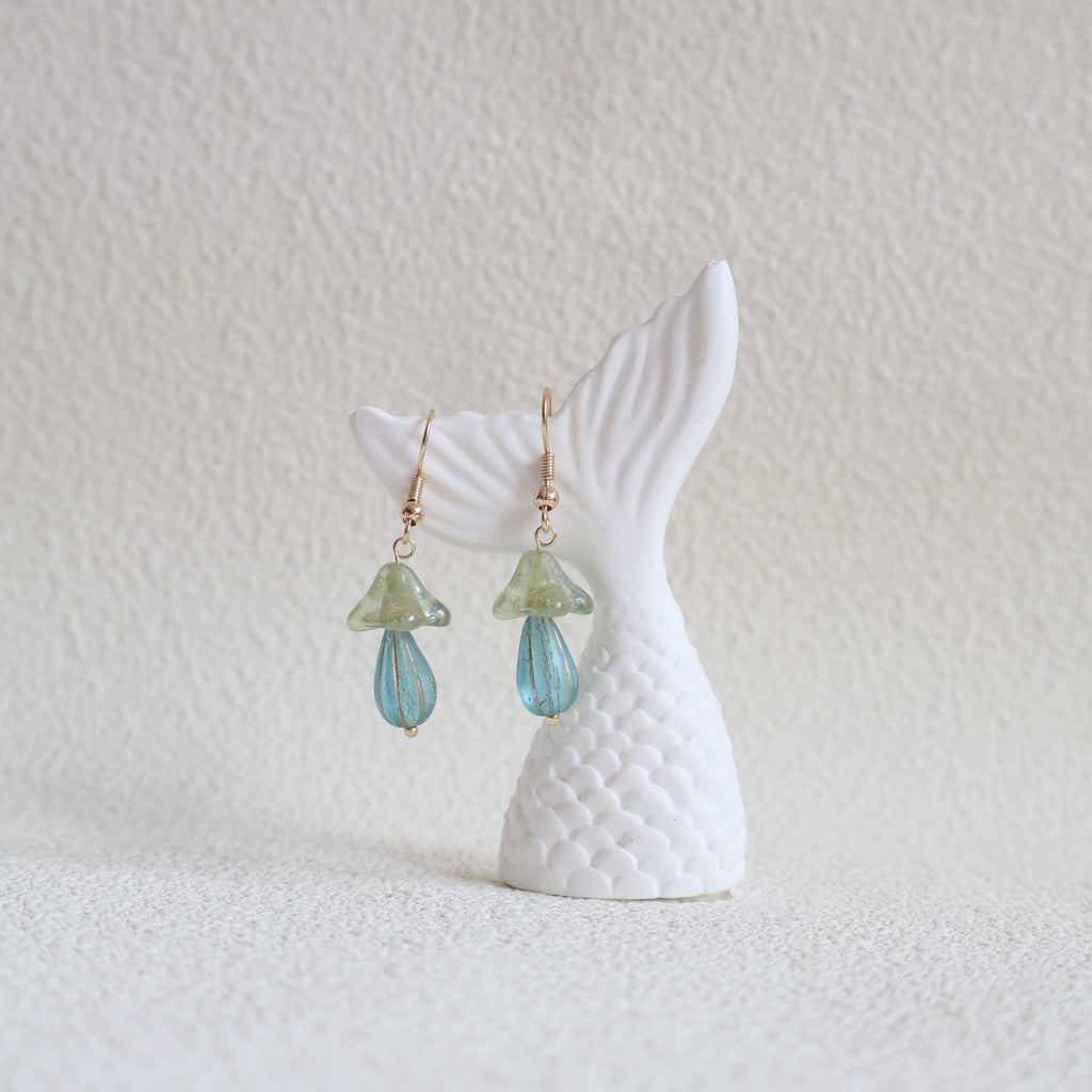Mermaid tail with green gemstone earrings on a textured white surface
