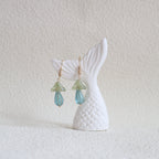 Mermaid tail with green gemstone earrings on a textured white surface