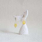 Mermaid tail earrings with a yellow bead on a textured white background