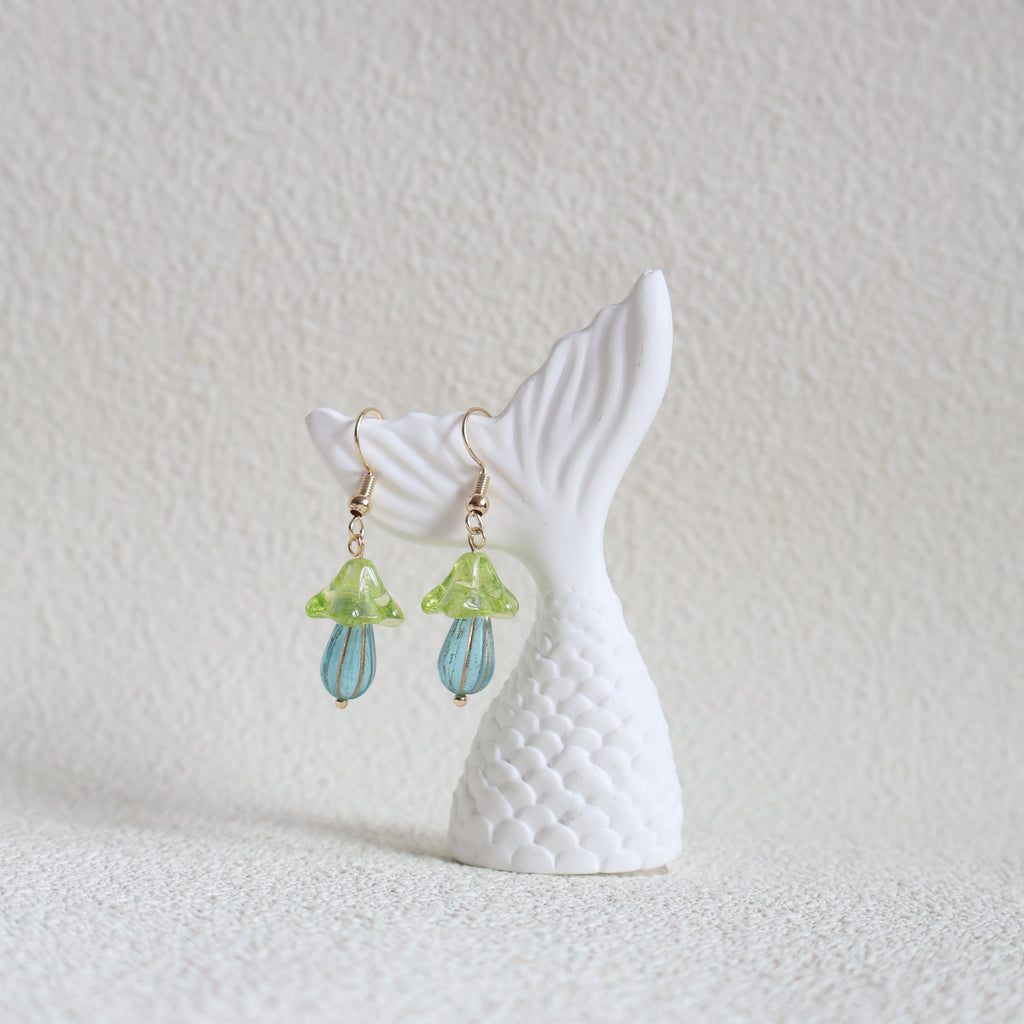 Mermaid tail earrings with green and blue accents on a textured white surface