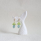 Mermaid tail earrings with green and blue accents on a textured white surface