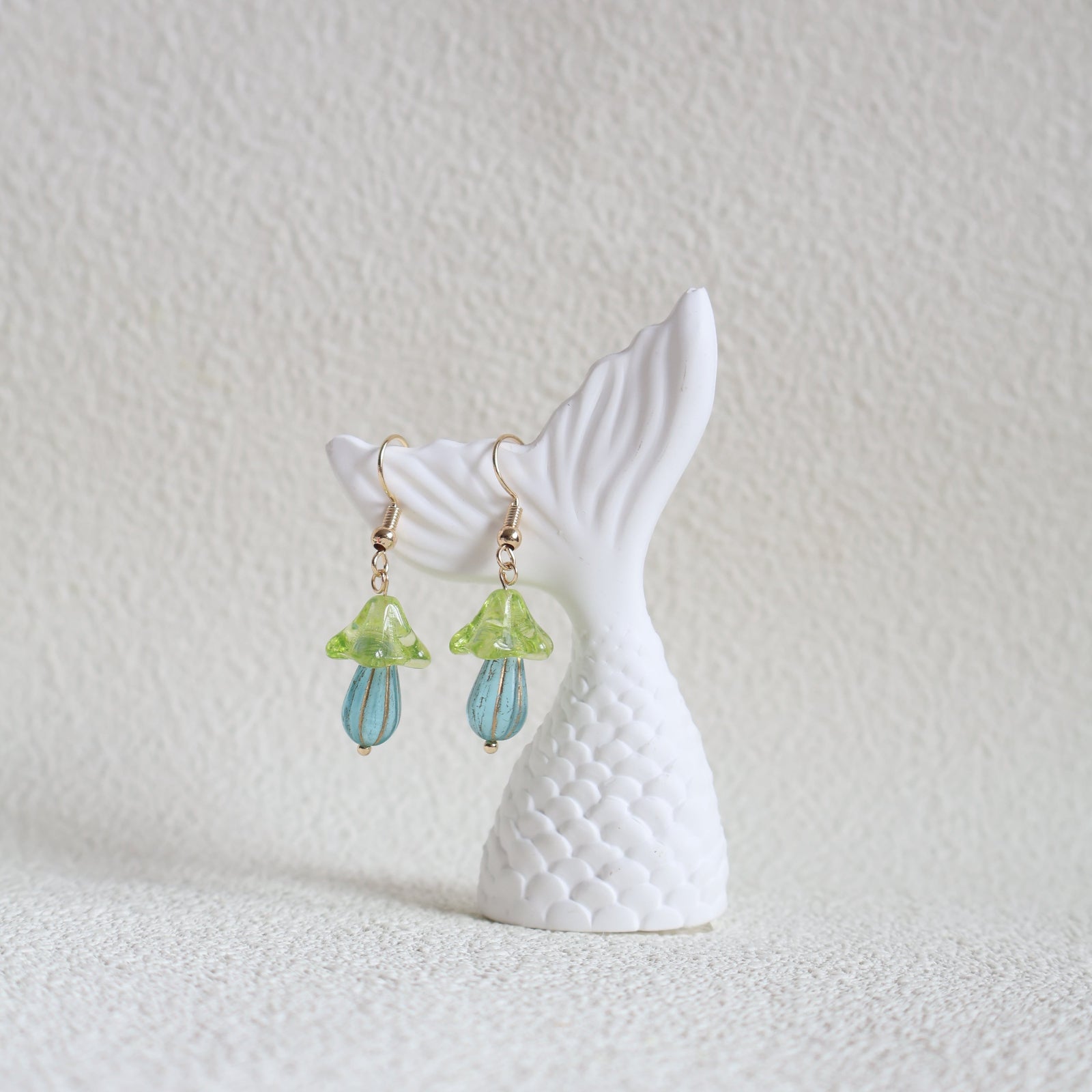 Mermaid tail earrings with green and blue accents on a textured white surface