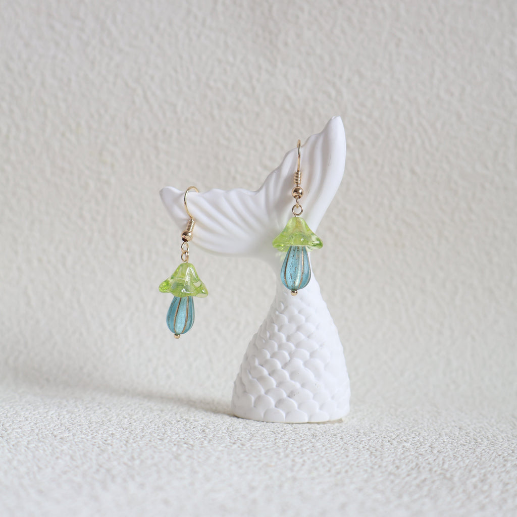 Pair of earrings shaped like whale tails with decorative elements on a light background