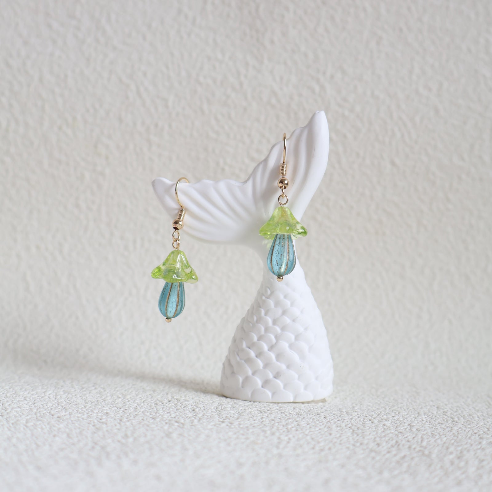 Pair of earrings shaped like whale tails with decorative elements on a light background