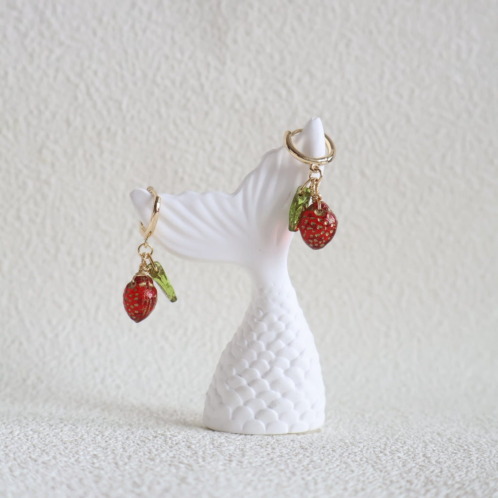 White seashell with red strawberry charms on a textured white background