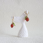 White seashell with red strawberry charms on a textured white background