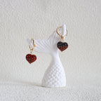 White fish-shaped earring with red and black heart charms on a textured white background