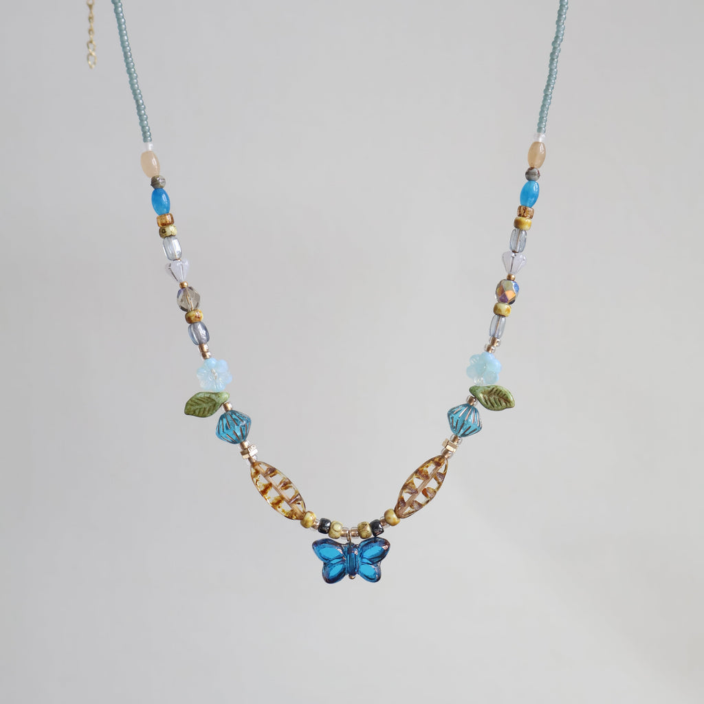 Beaded necklace with a blue flower pendant on a light gray background