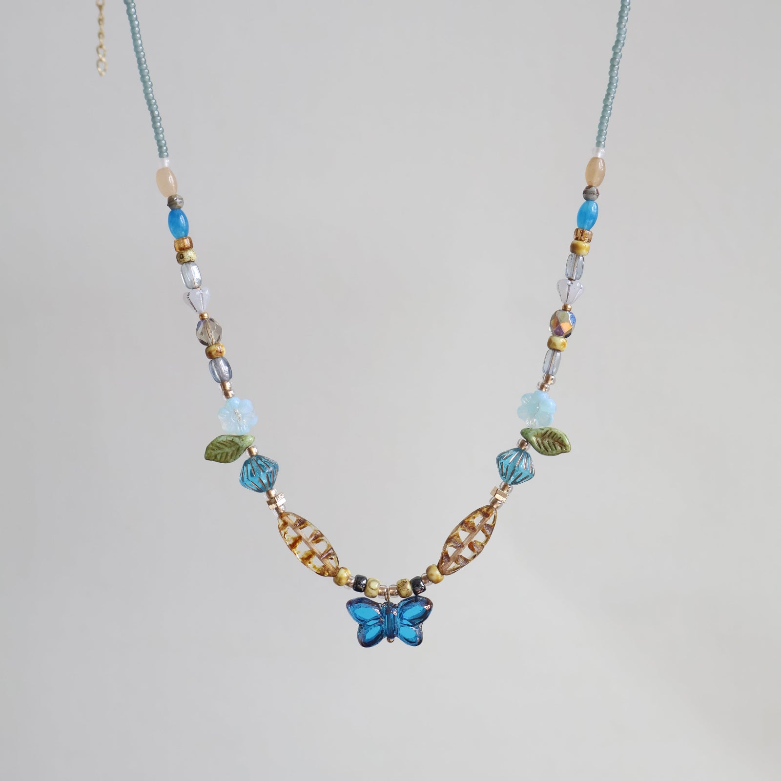 Beaded necklace with a blue flower pendant on a light gray background