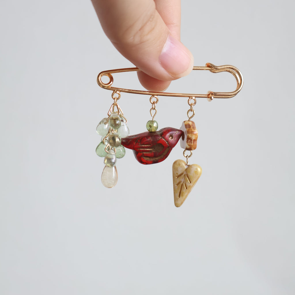 Hand holding a decorative brooch with gemstones and a butterfly charm on a light gray background