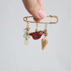 Hand holding a decorative brooch with gemstones and a butterfly charm on a light gray background