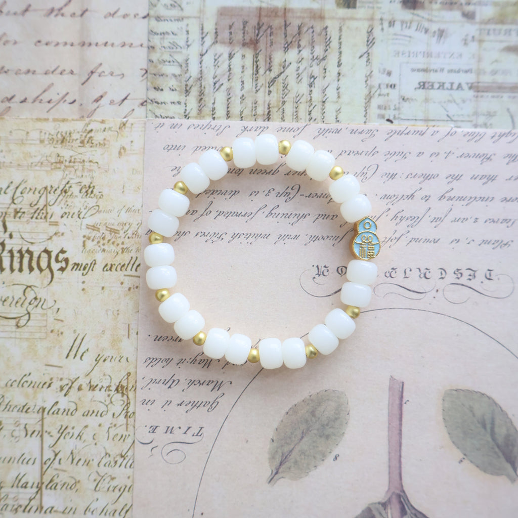 White beaded bracelet with gold accents on a vintage-style paper background
