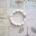 White beaded bracelet with gold accents on a vintage-style paper background