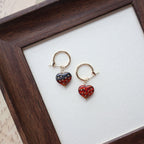 Pair of strawberry-shaped earrings on a white surface with a wooden frame.