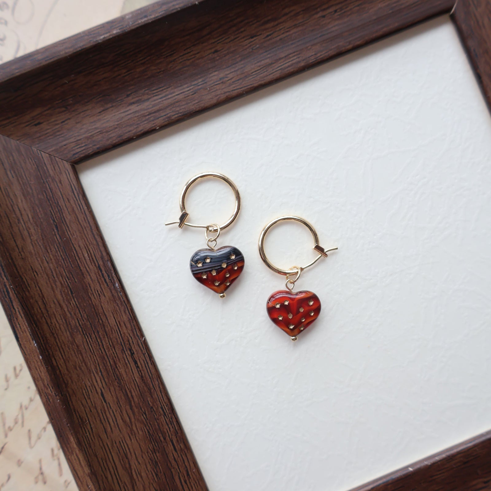 Pair of strawberry-shaped earrings on a white surface with a wooden frame.