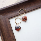 Pair of earrings with strawberry-shaped charms on a white surface with a wooden frame.