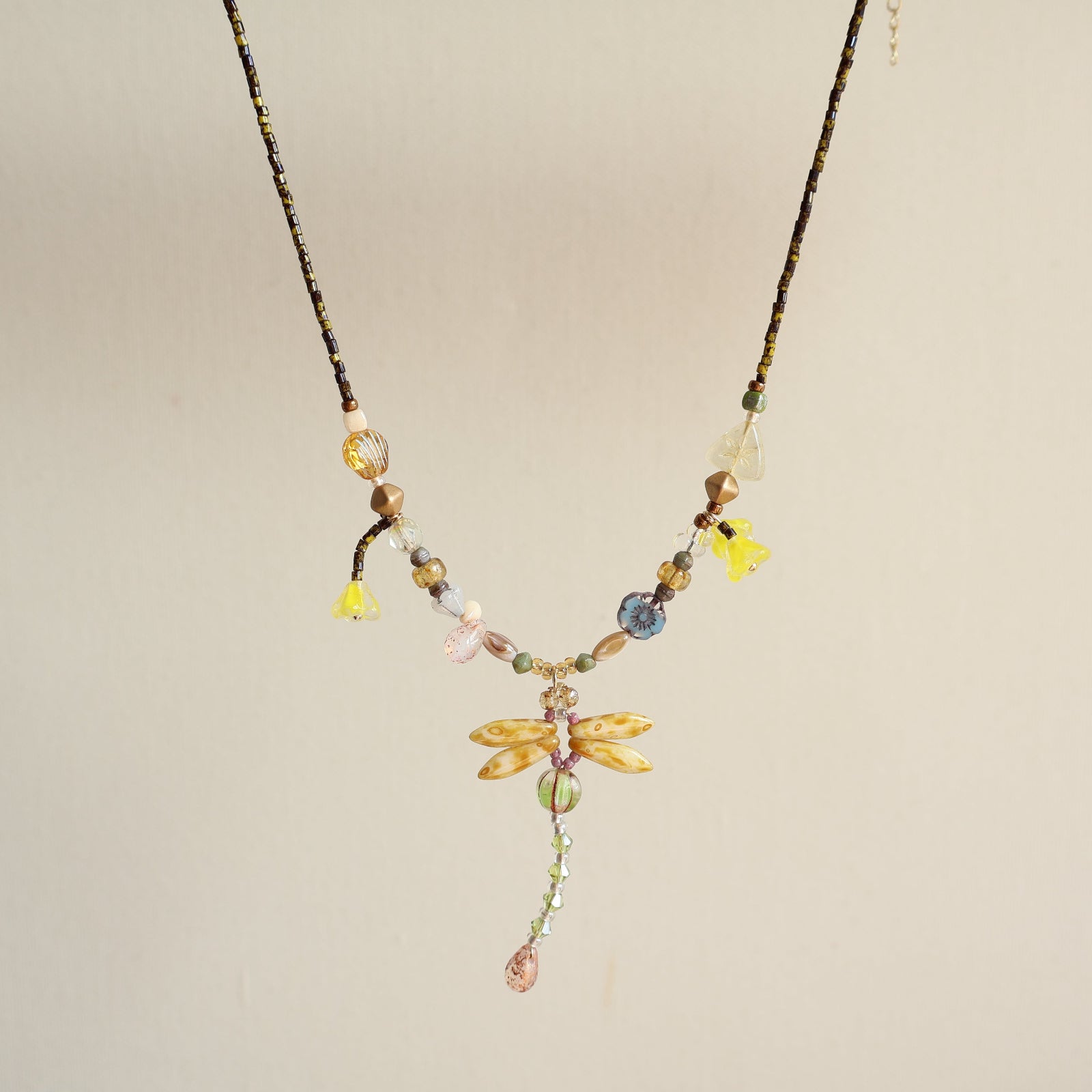 Necklace with dragonfly pendant and colorful beads on a beige background