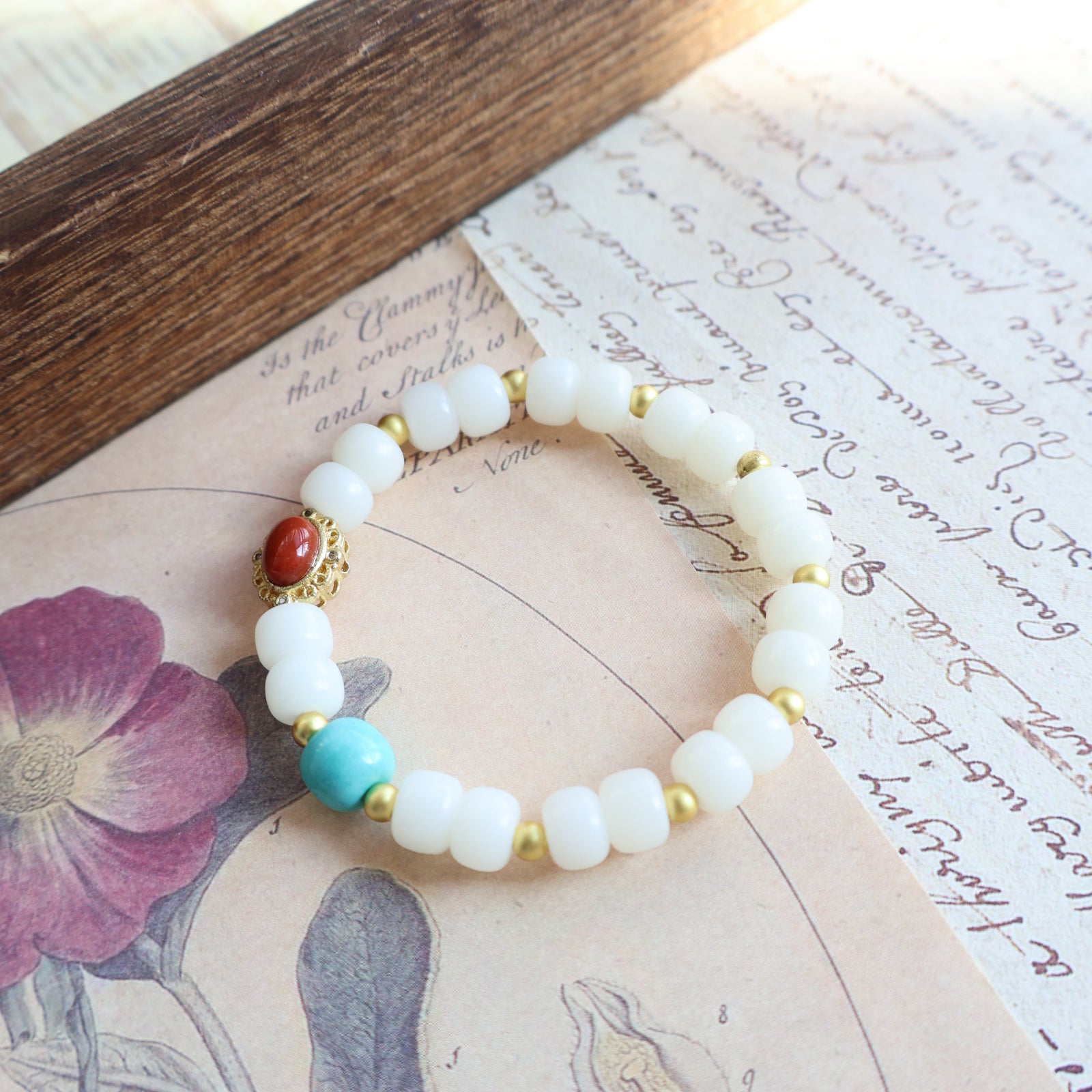 Beaded bracelet with white, gold, and turquoise beads on a vintage letter background