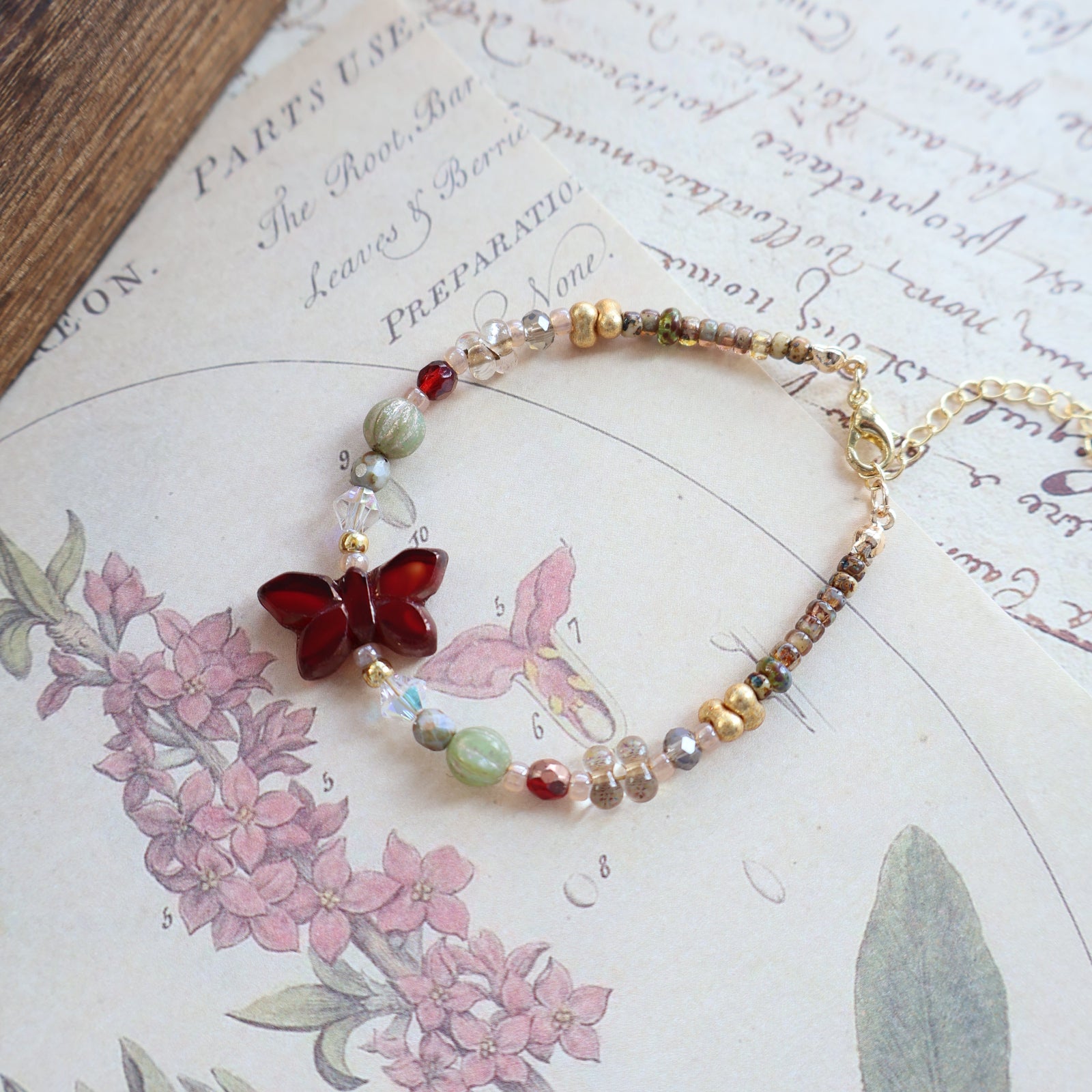 Beaded bracelet with a red butterfly charm on a floral and text background