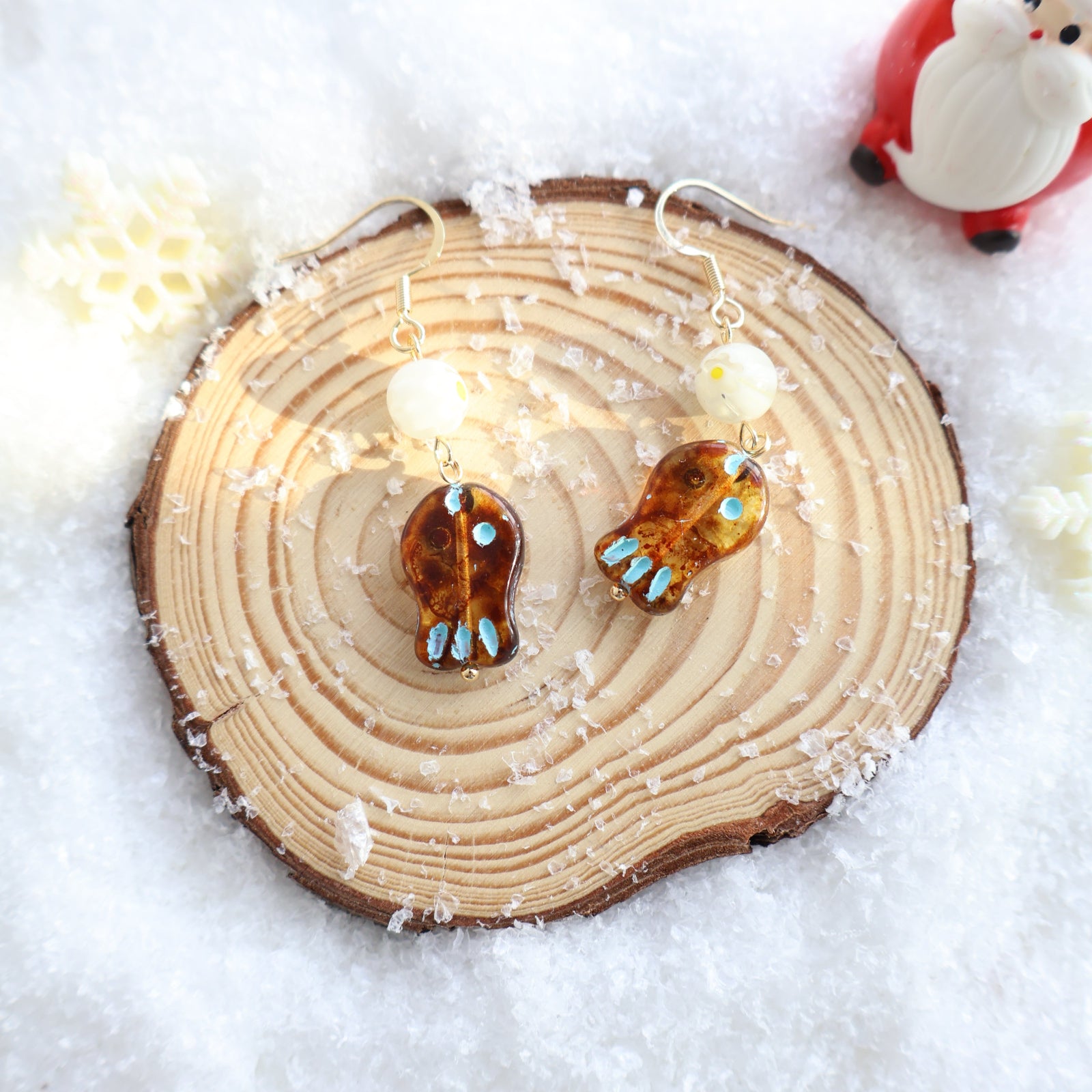 Two amber earrings with blue stones on a wooden slice in snow