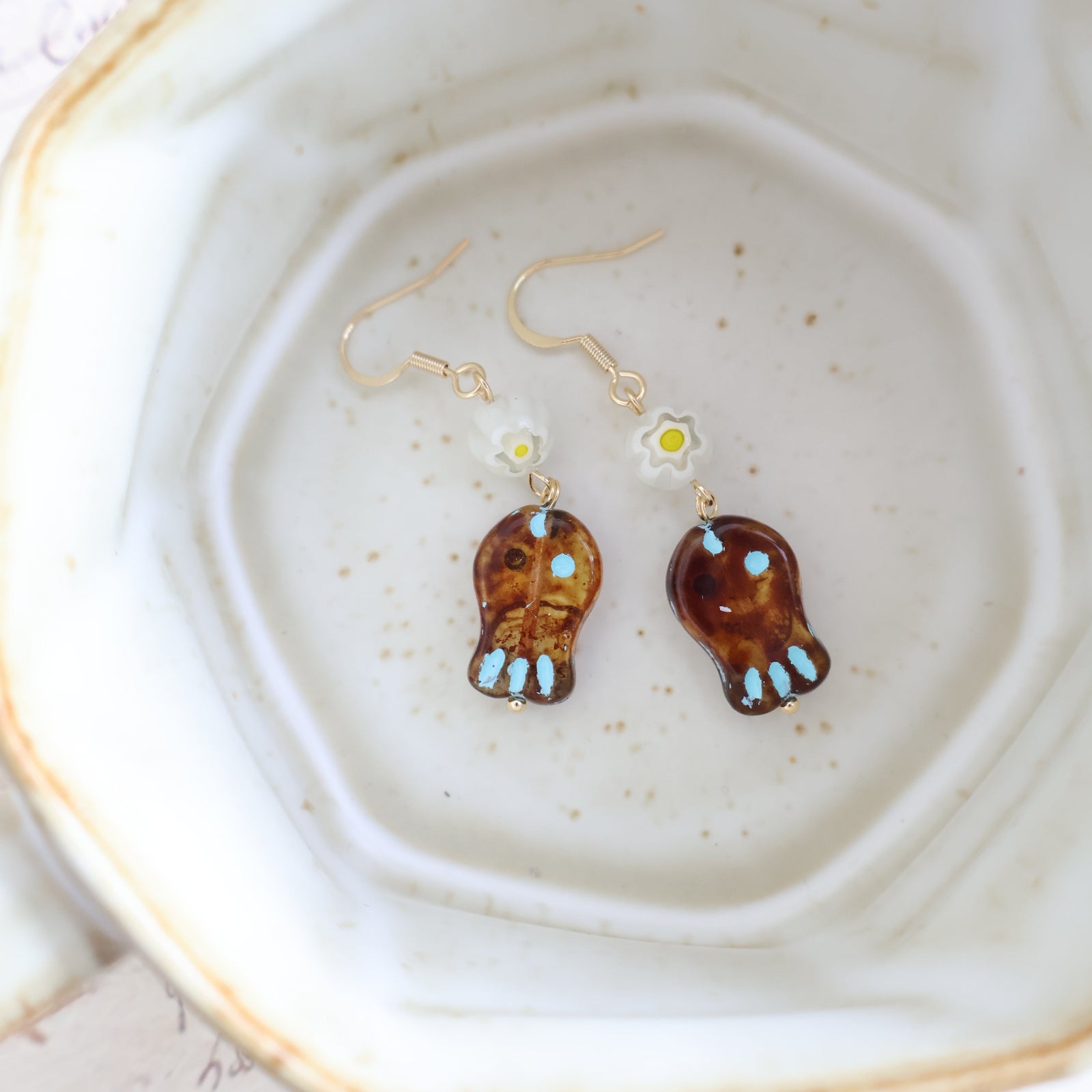 Two pairs of earrings on a textured ceramic plate.