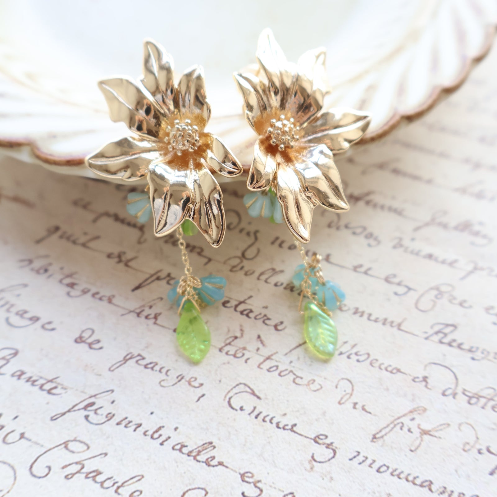 Gold floral earrings with green and blue accents on a textured surface